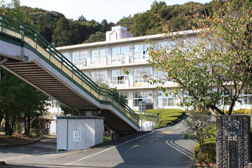 東山口小学校の外観。手前に校門と歩道橋のような階段があり、奥に校舎がある様子。