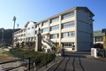大須賀中学校を正面玄関から撮影した外観写真で、正面玄関には時計塔がありそのすぐ奥に4階建ての白い校舎がある