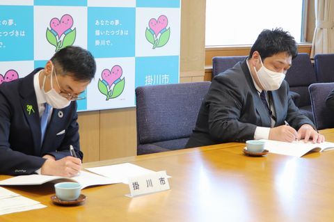 協定書にサインする野村さん(右)と久保田市長
