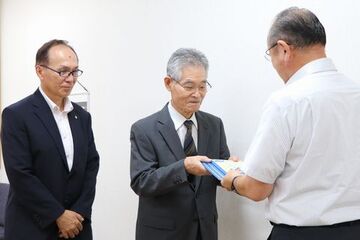 佐藤教育長(右)へガイドブックを手渡す石原さん(中央)