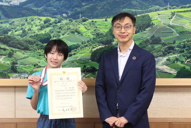 賞状とメダルを掲げる安川さん（左）と久保田市長