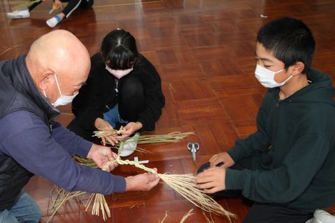 地域の方に手伝ってもらいながらしめ縄を作る児童