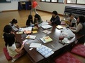机を囲んで、大人と子供たちが一緒に作品を作っている写真