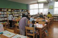 図書室で子供たちが、大人たちから折り紙の折り方を教わっている写真