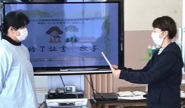 佐束幼稚園での講座の様子。モニターを挟んで立つ園長を保護者