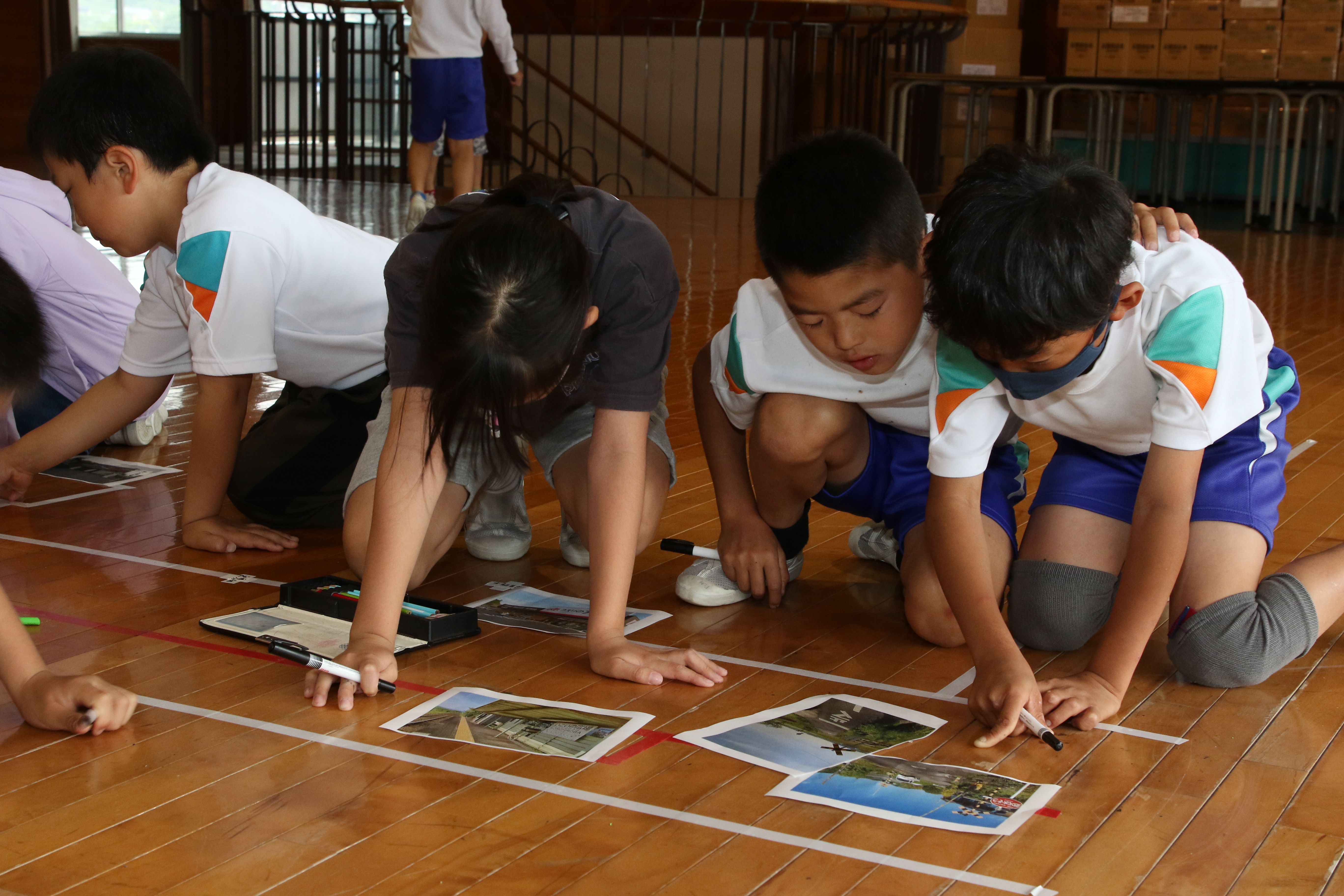 床に作成した大きな地図に地域の写真を貼り付ける生徒たち