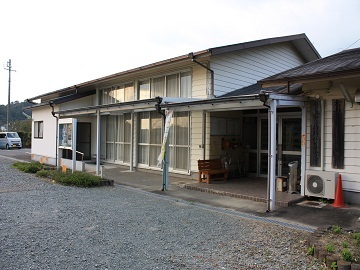 倉真地域生涯学習センターの外観写真で、平屋づくりの白い建物の入り口には庇があり、ベンチが置かれている