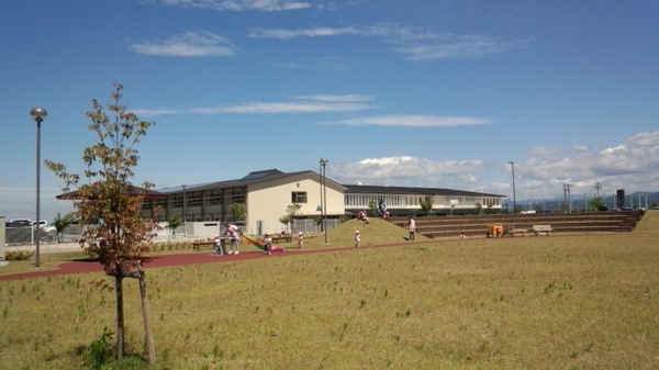 広い芝生が広がり、その奥に希望の丘の建物が見え、何人かの大人と子供が遊ぶ写真
