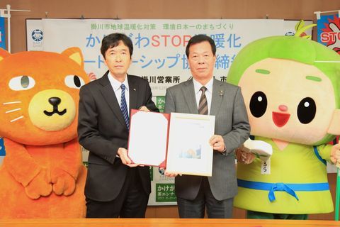 両脇にキャラクターを携え締結書を見せる伊藤所長と松井市長