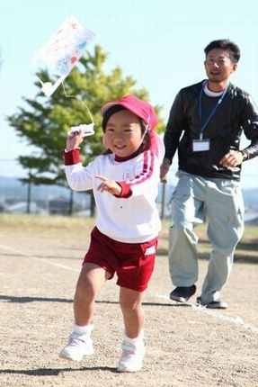 運動場で元気に凧揚げを楽しむ笑顔の親子の写真