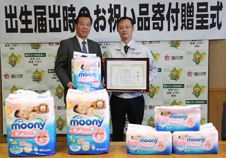 お祝い品の紙おむつを披露する松井市長と感謝状を受け取った三崎工場長