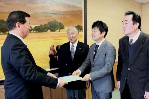 松井市長に笑顔で報告書を手渡す武井委員長等3名の様子