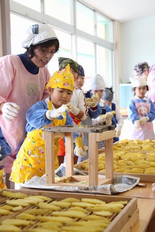 女の人と干し芋作りをしている園児達の写真