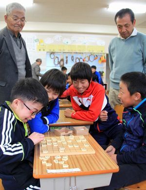 地域の先生が見守るなか将棋に熱中する児童たち。将棋を見ている子供たちも笑顔になっている写真。