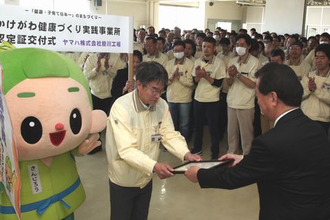 松井市長から認定証を受け取る高橋社長とそれに拍手をする従業員たち