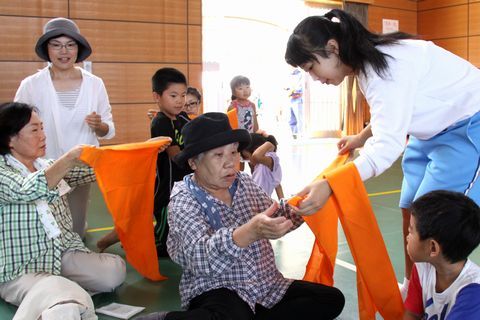 年配女性に三角巾法を熱心に指導する中学生とまわりでその様子を見ている他の参加者