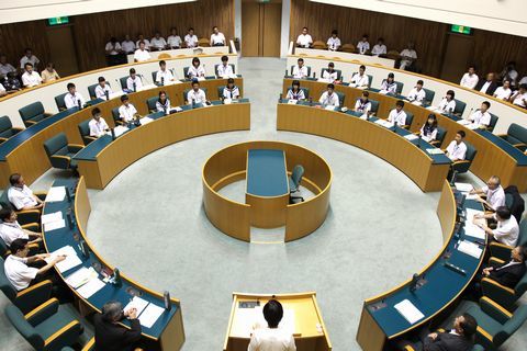 円状に机が配置された市議会議場で中学生と議員が議会を開いている