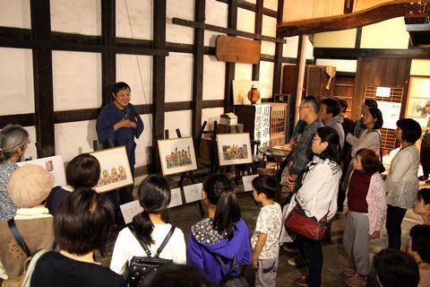 絵本の原画を並べ解説する川端誠さんと原画の前に並び解説を聞く参加者