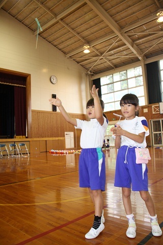 体育館で体操着を着た女子小学生二人が竹とんぼを飛ばしている