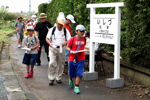 石津駅と書かれた駅看板の前を通過する参加者ら