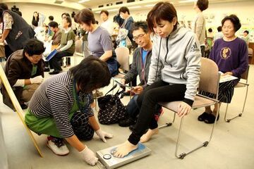 椅子に腰を掛けて足指力測定を受ける参加者と測定を行うスタッフ