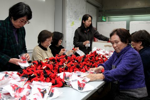 机の上にある大量のさるぼぼの袋詰め作業をする会員たち