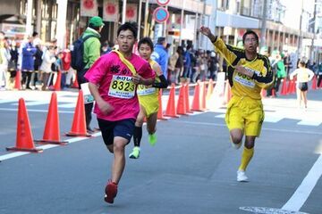 体にかけたたすきを渡す準備をしながら走る選手たち3人