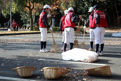 熊手を使い駐車場の落ち葉を一箇所に集める生徒たち