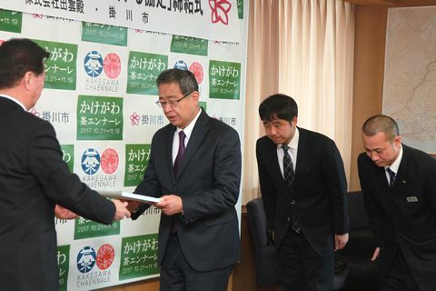 松井市長から協定書を受け取る専務の岡野壮一郎さんとその後ろで頭を下げる男性二人