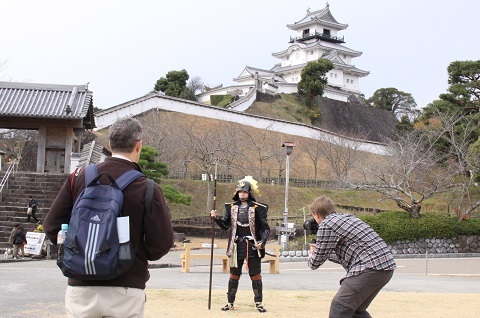 掛川城を背景に、甲冑を試着したエバンスさん（男性）を撮影するマーストンさん（男性）