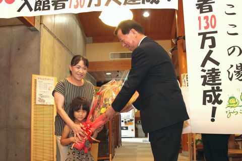 130万人達成の垂れ幕の横で松井市長から花束を受け取る杉山さんと彩菜さん