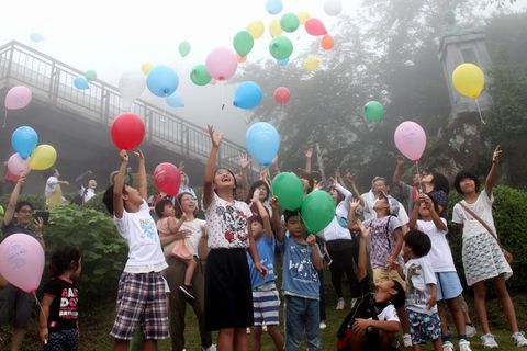 粟ヶ岳山頂からメッセージ付きの風船を空に向かって飛ばす参加者たち