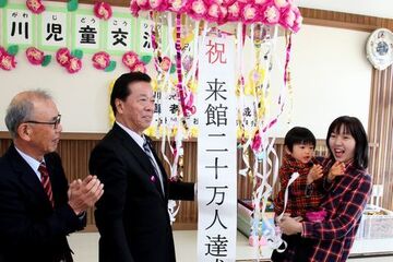 20万人目の来館者となった国府五月さん・眞智さん親子。割れたくす玉の前で笑顔になっている写真。