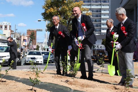 スコップを持ち笑顔で茶の苗木を植樹するサルッチ楽団総裁らの写真