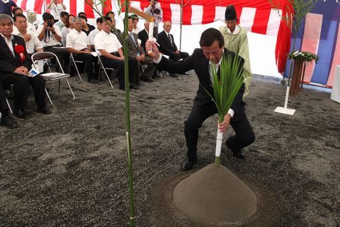 市長が左手で盛り砂の真ん中に刺した植物を支えながら右手に持った鎌を振り上げる鎌入れの儀の様子