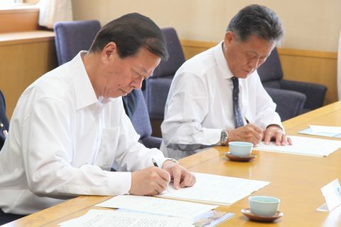 協定書にサインする手前の松井市長とその奥の原田益夫社長