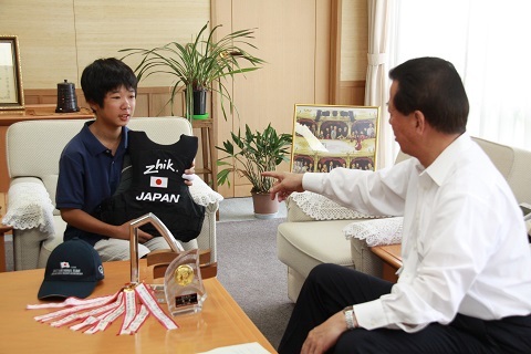 日の丸がついた黒いベストを市長に見せる遠藤貫太郎さんとそれを指差す松井市長