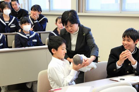 小川教授から人形を渡され新生児の抱き方を学ぶ生徒の様子