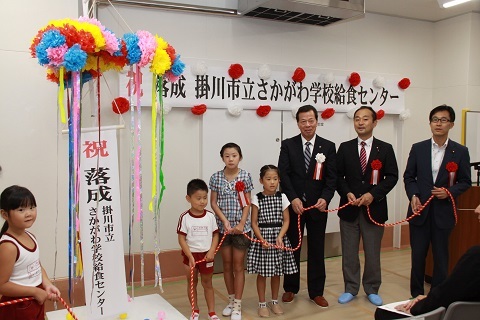 くす玉を割り新たな学校給食センター完成を祝う関係者の写真
