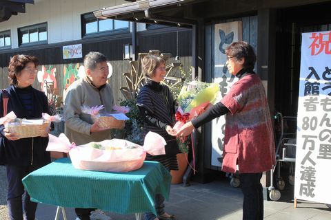 80万人目の入館者となった坪井さんと前後賞の植田さん、山内さんが花束を受け取る様子