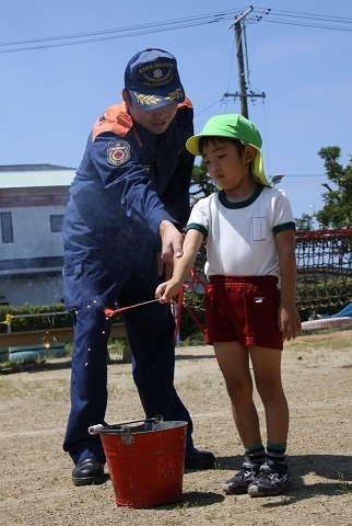 近くに消火用のバケツを置き、消防士と一緒に手持ち花火をする男児