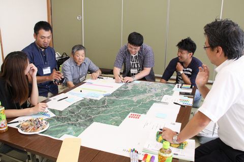 大きな地図を机の上に広げ、地域の魅力を確認し合いメモをとっている参加者らの写真