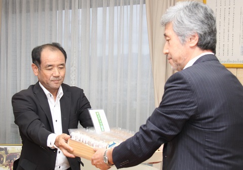 大木委員長へ木箱に入ったたくさんの木製コースターを寄贈する鈴木社長の写真