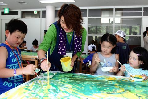テーブル一杯に広げられた大きな麻布に緑色で思い思いの絵を描く子どもたちと船井さん