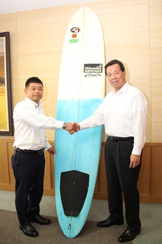 サーフィンボードを挟んで松井市長と藤田さんが握手している