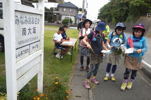 南大坂駅跡地の駅看板の横を歩く女性参加者らの写真