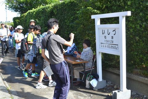 当時のプラットフォーム跡が残る石津駅跡地の駅看板を写真に撮る参加者の写真