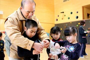 地域の方に手を添えてもらいながらひもの巻き方を教わる園児たちの写真