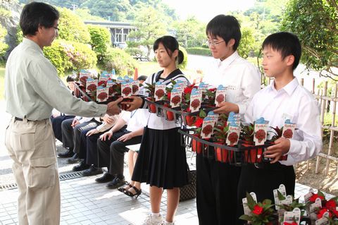 竹林副場長(左)から赤い花びらが美しいサンパチェンスの苗を受け取る生徒代表