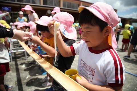 流しそうめんで上手にそうめんをすくう笑顔の園児